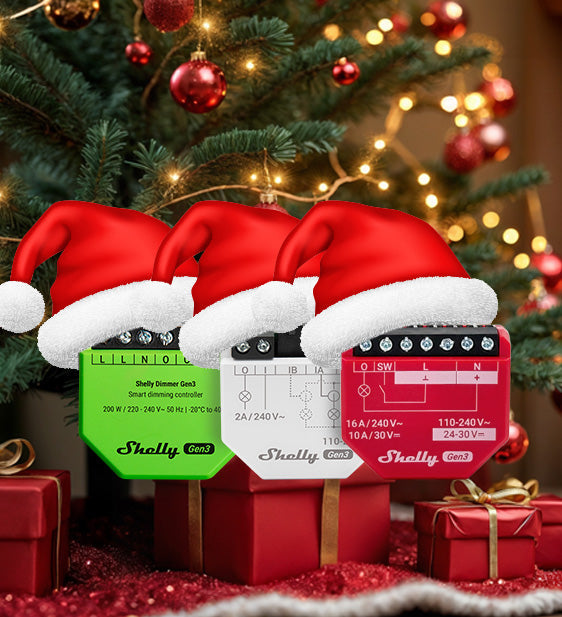 Three Shelly smart dimmer devices wearing Santa hats are displayed in front of a decorated Christmas tree, with red and gold ornaments and wrapped presents underneath.