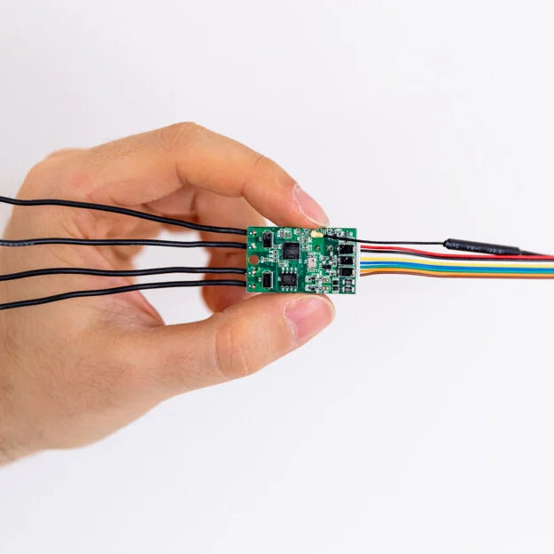 A hand holds a Shelly Uni by Shelly USA—a small green circuit board with multiple colorful wires and a smart Wi-Fi module for sensor control—set against a plain white background.