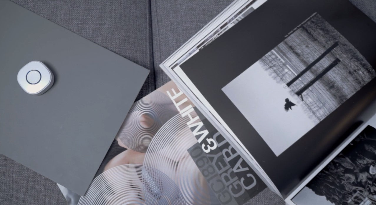 A gray remote on a closed laptop sits beside open black-and-white photography books and magazines on a gray fabric surface.