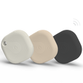 Three square Bluetooth tracking devices in white, beige, and black, each with rounded edges and a circular pattern, are displayed standing upright against a plain white background.