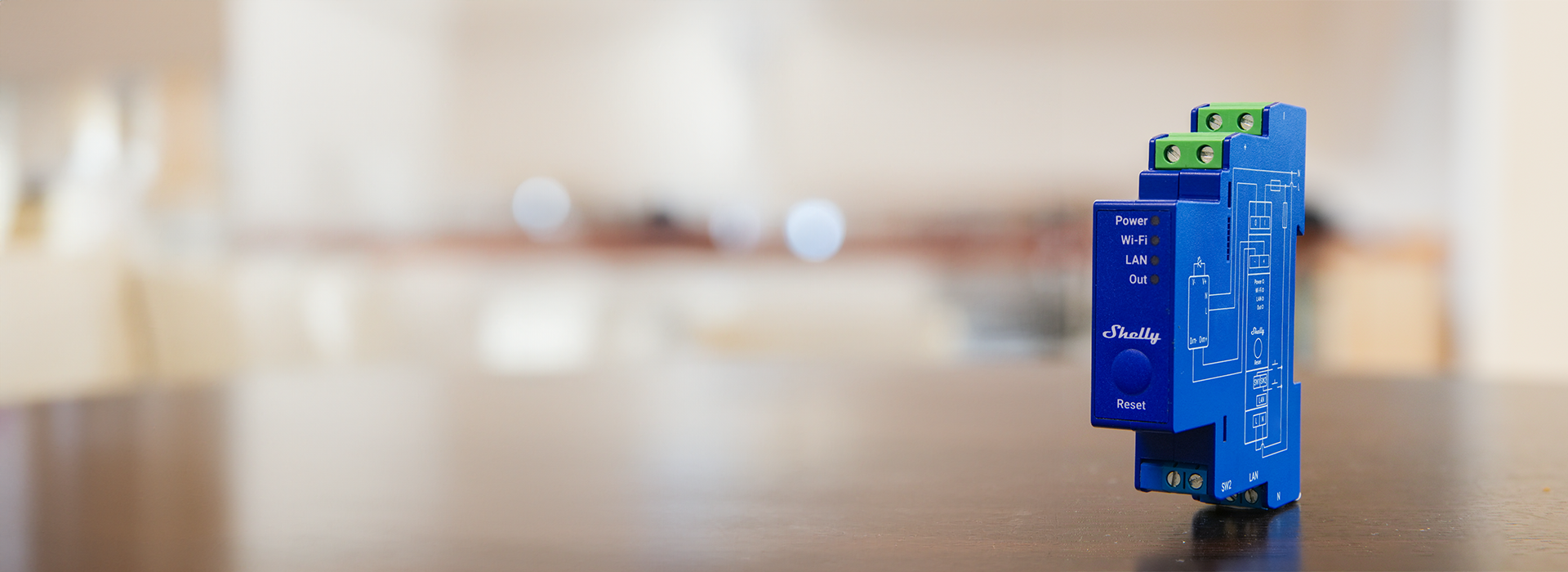 A blue Shelly Wi-Fi relay switch device stands upright on a blurred brown tabletop, with a neutral, softly lit background.