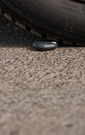 A car tire is about to roll over a small, dark, oval-shaped object lying on a rough asphalt surface.