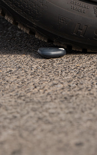 A car tire is about to roll over a small, dark, oval-shaped object lying on a rough asphalt surface.