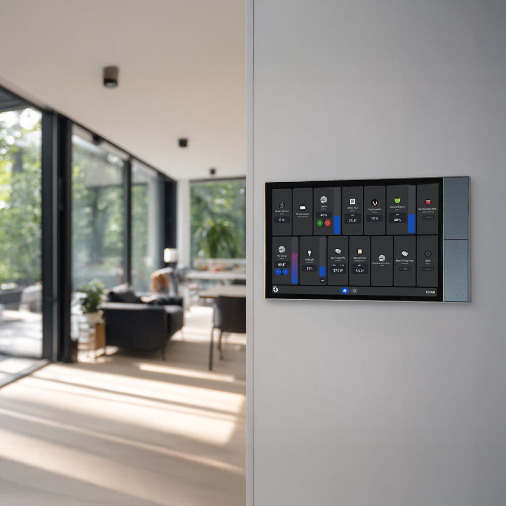 The Shelly Wall Display XL by Shelly USA is mounted on a wall; in the background, a modern living room with large windows and natural light can be seen.