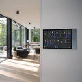 The Shelly Wall Display XL by Shelly USA is mounted on a wall; in the background, a modern living room with large windows and natural light can be seen.