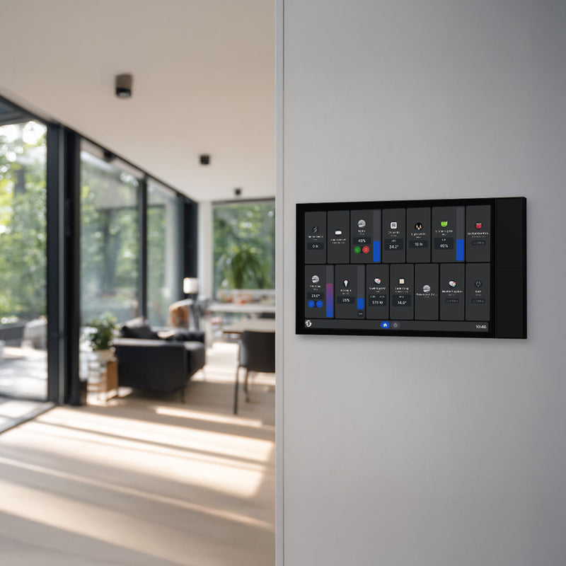 The Shelly Wall Display XL Black by Shelly USA is mounted on a white wall, with a modern living room featuring large windows and stylish furniture visible in the background.