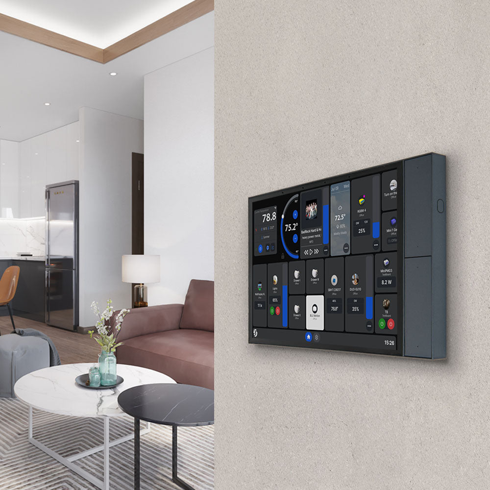 The Shelly Wall Display XL by Shelly USA is mounted on the wall, showing multiple controls. Behind it, a stylish living room with a sofa, coffee table, and an open kitchen featuring a refrigerator and lamp is visible.