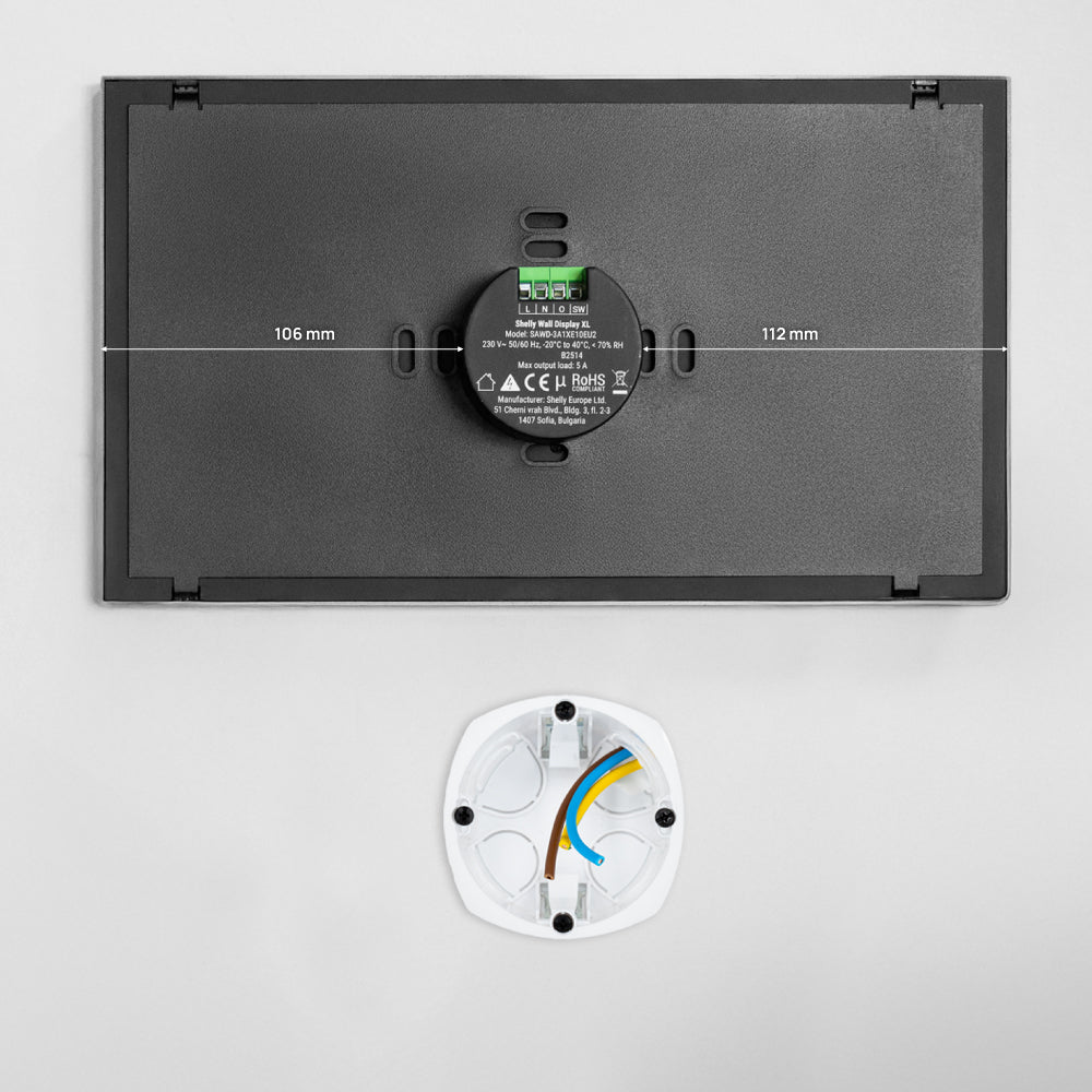 The Shelly USA Shelly Wall Display XL list is a rectangular black wall-mounted device with labels, a central round element, and measurements of 106 mm by 112 mm, shown above a white circular base with visible colored wires.