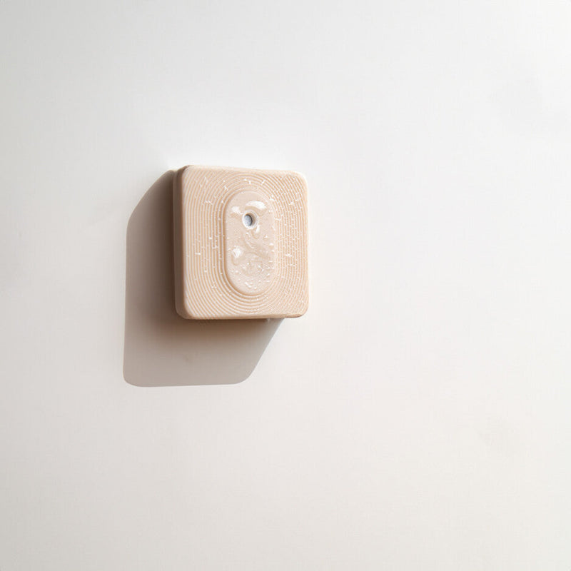 The Shelly Shelly BLU H&T ZB Mocha, a beige square device with a clear center and subtle textured surface, is mounted on a white wall and casts a soft leftward shadow.