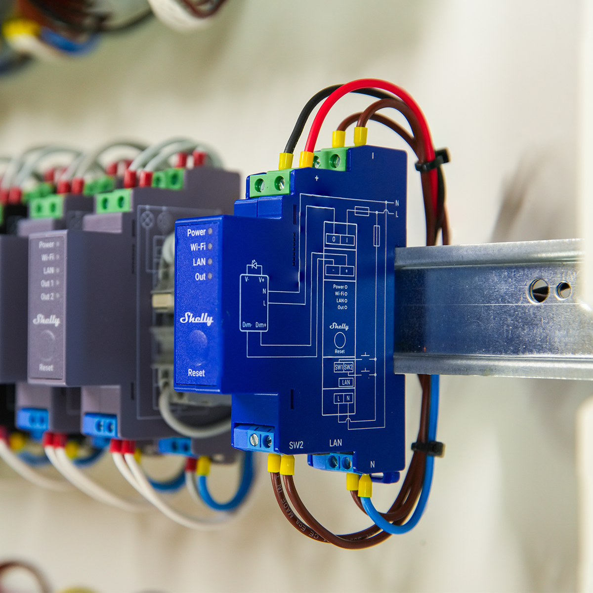 A close-up view of an electrical relay device mounted on a metal rail, with detailed wiring and circuit diagram visible on the blue casing, surrounded by connected cables and adjacent devices.