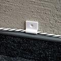 A Shelly Europe Shelly Cable Bracket from the 10-pack secures a twisted cable with a screw hole to a textured gray wall above dark carpet flooring.