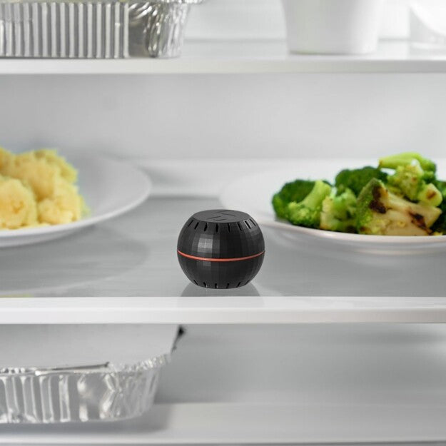 A Shelly USA Shelly H&T Black, featuring a built-in home humidity monitor, sits on a refrigerator shelf between plates of vegetables and mashed potatoes.