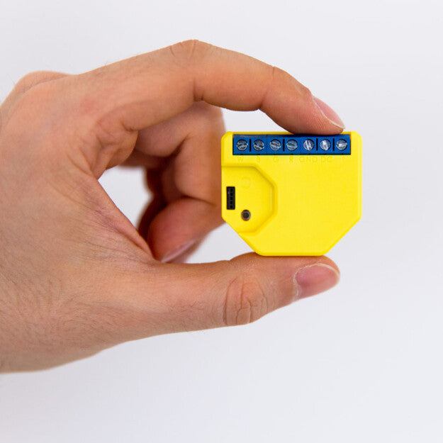 A hand holding the Shelly USA Shelly RGBW2, a compact yellow device with blue screw terminals and a front micro-USB port—perfect for Wi-Fi relay setups or controlling LED smart strips in smart home projects.